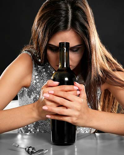 грустная женщина сидит за столом и держит в руках бутылку вина