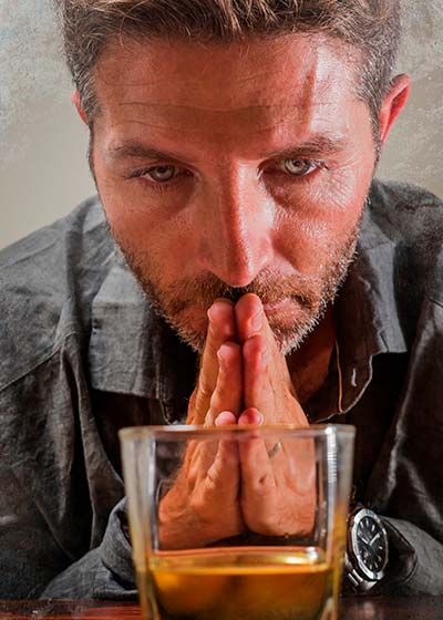мужчина сложил руки в молитве перед стаканом с алкоголем
